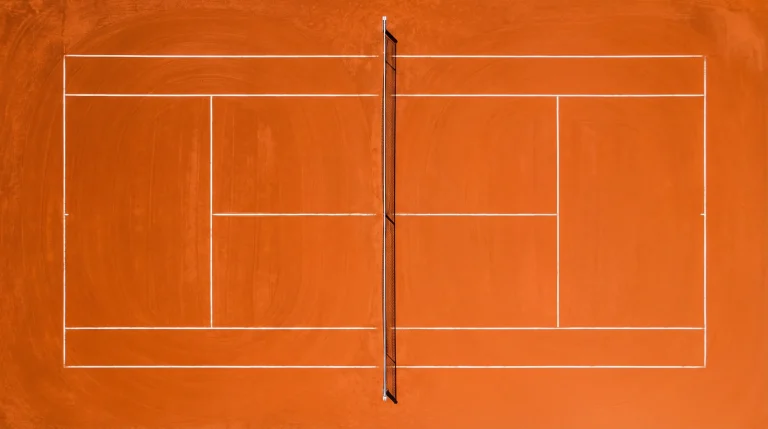 Vue en plongée d'un court de tennis en terre battue avec les lignes blanches et le filet au centre