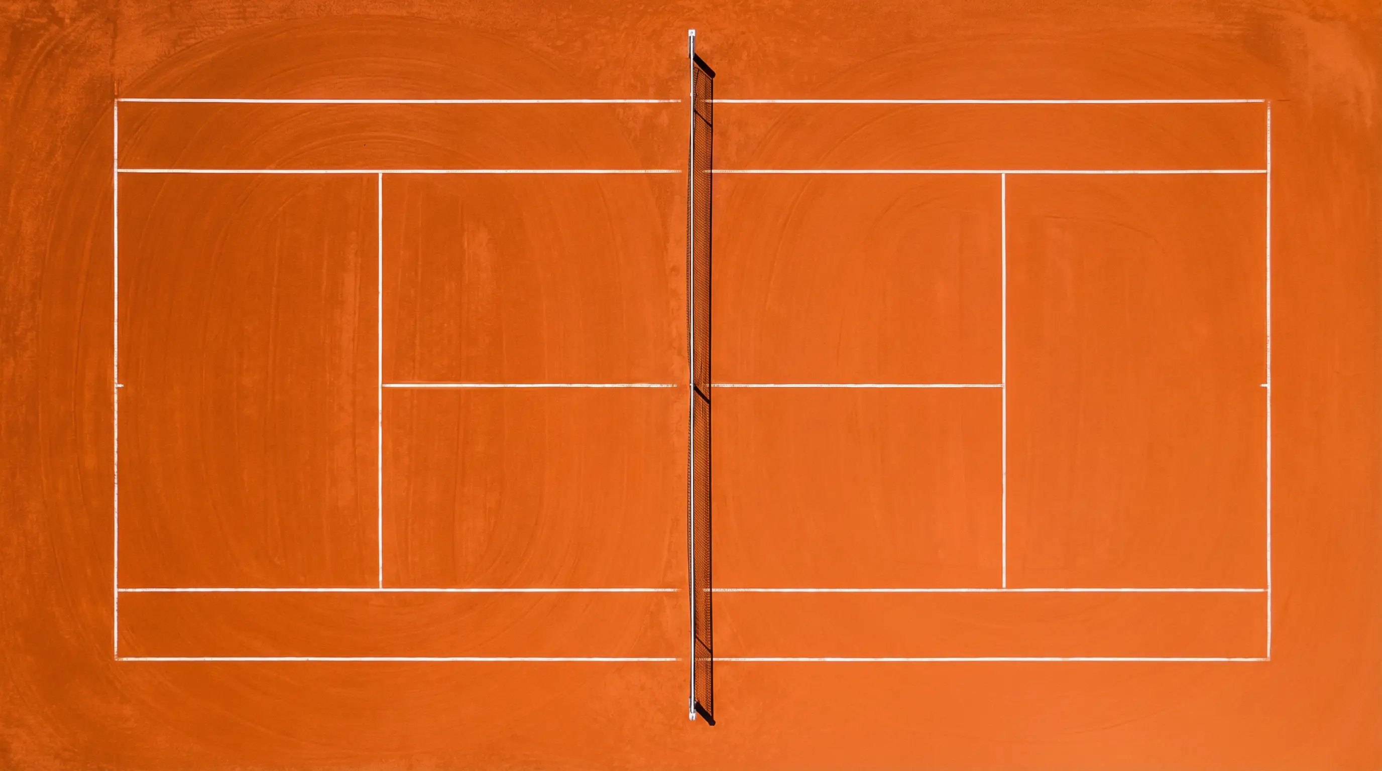 Vue en plongée d'un court de tennis en terre battue avec les lignes blanches et le filet au centre