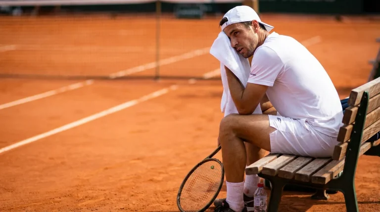 Joueur de tennis essuyant la sueur sur son front entre deux sets sur un court en terre battue